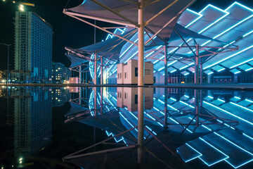 View of the colorful illuminated building and night city with modern architecture reflecting on the water surface
