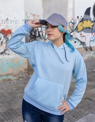 Blue haired Teenage girl in blue hoodie and baseball cap staying against graffiti wall