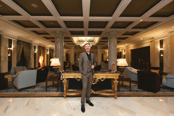 Fototapeta premium Businessman man in a classic stands in the luxurious interior of the hotel and shows a thumbs up.