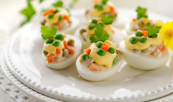 Hard- boiled eggs divided into halves and stuffed with traditional  vegetable salad with mayonnaise served on a white plate close up view. Easter food