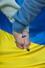 male and female hands together, on them a heart painted in yellow and blue colors of the Ukrainian...