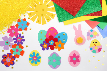Composition of colorful Easter eggs, flowers, sun, chicken, rabbit from multi-colored paper, step by step. Child makes crafts his own hands. Easter DIY handmade art creativity. Top view, copy space