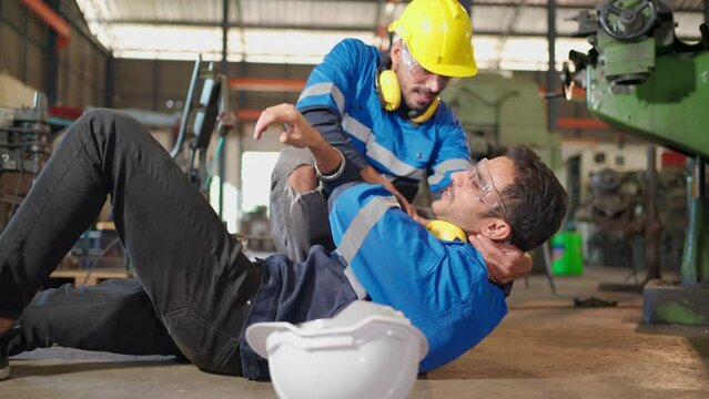 Man labor worker had accident on the floor at the production line of CNC machine factory. Engineer man walk to that area and support him on injured. Safety in industrial factory. Injury at work