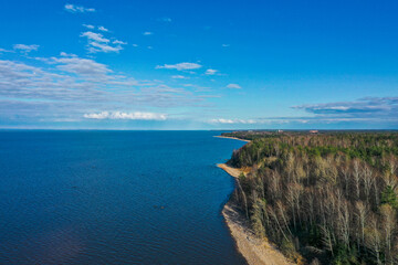 Aerial view of the coastline of the Gulf of Finland. Sandy coast and forest belt. Treetops, blue sky.