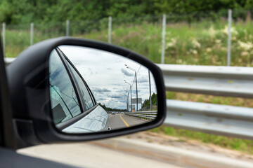 Close-up of a car's rear-view mirror, which reflects the road and other cars. Selective focus.
