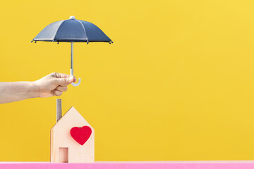 Woman hand hold open the black umbrella for protect to home with red heart on bright yellow color...