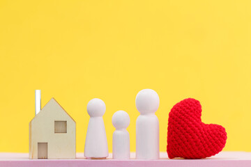 Houses model and red heart and wooden family model put on the pink foam on bright yellow color background in the office, The buying a new real estate as a gift to family or the one loved concept.
