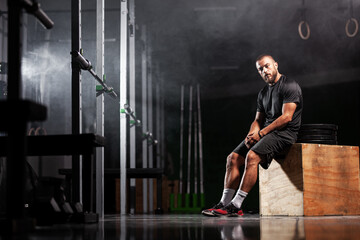 Muscular athlete posing with weightlifting equipment. Smoke background