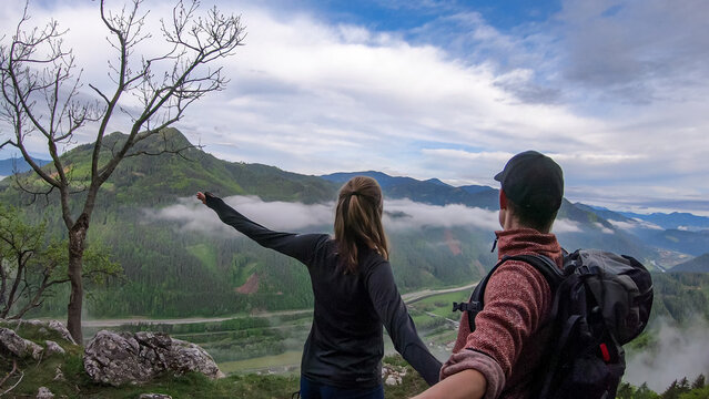Couple admiring the scenic view from mount Roethelstein near Mixnitz in Styria, Austria. Landscape of green alpine meadows and a  village in the valley of Grazer Bergland in Styria, Austria. Selfie