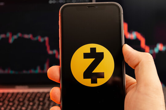 Zcash ZEC cryptocurrency logo on the screen of smartphone in mans hand with downtrend on the chart on a red light background, February 2022, San Francisco, USA.