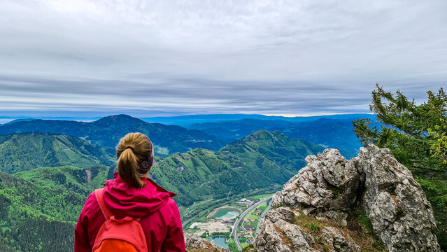 Woman admiring the scenic view from the summit of mount Roethelstein near Mixnitz in Styria, Austria. Landscape of green alpine meadows and hill in the valley of Grazer Bergland in Styria, Austria.