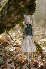  Portrait of a cute blonde doll cat with green eyes dressed in a  jacket and nice dress standing next to a tree.