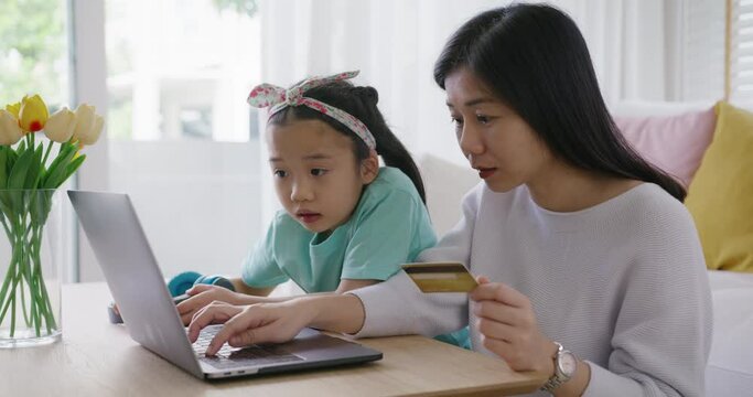 Young girl little kid help mom pay school charge tuition term fee or tax bill on web social media app relax smile at home sofa. Asia people happy playful fun buy gift card on online shop on laptop.