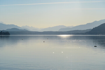 View on Woerthersee in Poertschach in Carinthia, Austria.The calm surface of the lake is reflecting the mountains, sunbeams and clouds. Clear and sunny day. Karawanks mountain range. Alps, Lake Woerth