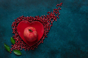 Pomegranate in the red heart shape plate on the blue background. Top view, close up