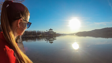 Happy woman standing on the pier at beautiful Woerthersee in Poertschach, Carinthia, Austria. Scenic lake landscape surrounded by Alps. Serenity. Fresh and clean air. Reflection in Lake Woerth