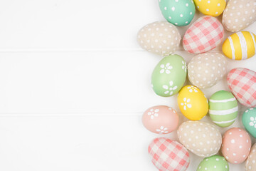 Easter side border with farmhouse style cloth and pastel colored eggs over a white wood background. Above view with copy space.