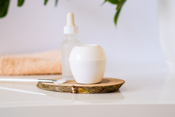 White jar of skin cream and a bottle with a dropper from serum with a brush for applying a face mask. Still life minimalistic beauty cosmetic template. Organic eco friendly products on a wooden plate.