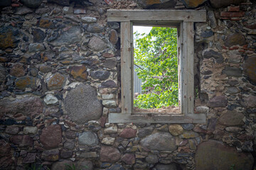 old durable resistant wall build in granite boulders and rocks with massive wooden window frame without glass