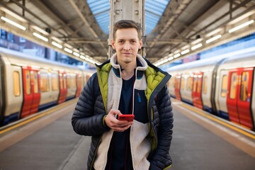 man standing on a platform looking at his phone waiting for a train