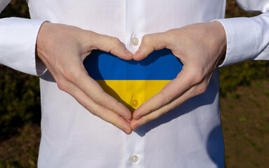 man holidng his hands in heart shaped on white shirt with ukraine flag colors support concept