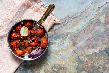 Roasted tomatoes with onion and thyme in a pan. Top view with copy space. Rustic food photography.