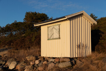 White wooden beach hut on rocky slope in the evening sun.