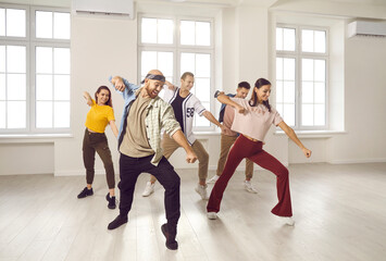 Happy young people in casual streetwear dancing together in bright studio. Energetic smiling millennial dancers crew or team training exercising, prepare for contest. Hobby and entertainment.