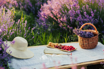 Picnic in lavender field with wine, berries and croissants. Wicker basket with bouquet of lavender. Romantic picnic in lavender field background.