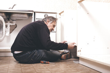 Older man disassembling apartment kitchen out of service