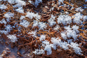 Beautiful pattern of snowflakes on the spring ground. Snow glitters in bright sunlight. Natural pattern in brown and white colors. 