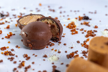 Bombom de chocolate com amendoim cortado ao meio sobre fundo branco com granulados doces ao redor