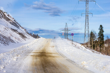 Fototapeta na wymiar Winter road in the mountains, traveling through snowy mountainous terrain on a sunny frosty day.