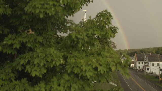 Aerial shot descending rainbow beyond church by roadside Monson Town 