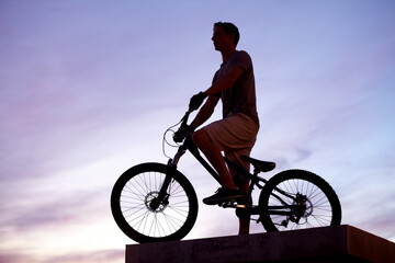 King of the city. Silhouette shot of a man riding his bike at dusk.
