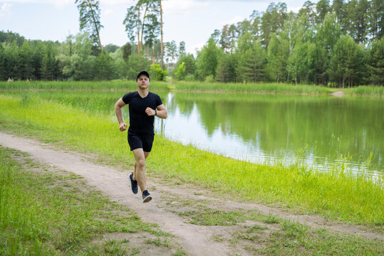 man in black clothes and cap running along lake in summer forest