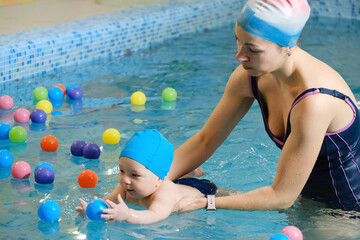Early age swimming in pool. Baby boy trained to swim in water. Happy child with trainer woman in...