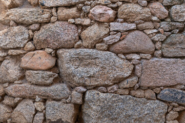 A old stone wall in which there are stones of different sizes, textures and colours, most of them are brown. 