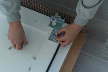 Hands hold screws to attach iron fittings to white wooden boards on the floor, on top of cardboard.