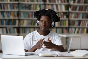 Concentrated young African American male student in headphones looking at computer screen,...