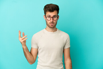 Fototapeta premium Young caucasian handsome man isolated on blue background making doubts gesture