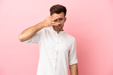 Young caucasian handsome man isolated on pink background covering eyes by hands and smiling