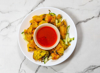 deep-fried cucur udang prawn fritters with chili sauce served in white dish isolated on marble background top view