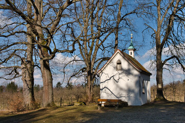 Fototapeta na wymiar Christliche Kapelle in der Natur / Wald mit Bäumen im Frühling und blauem Himmel