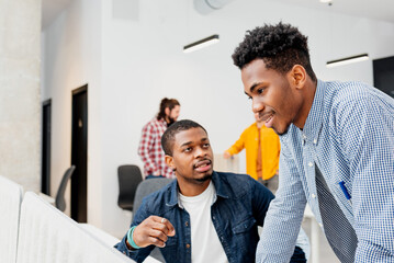 two black male college students talk and work together on a college project in a campus study room. young entrepreneurs.