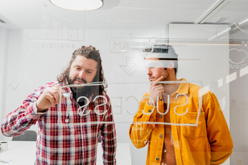 two creative white men draw a business strategy plan on a glass board to achieve the success of...