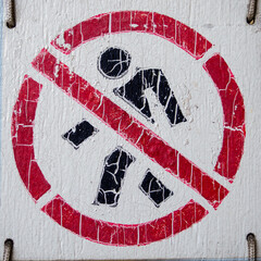 The symbol of a person is crossed out in a red circle. Old with cracked paint. no entry.