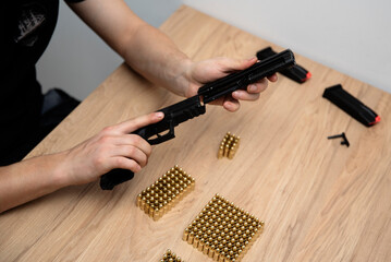 Mężczyzna wkłada lufę broni do mechanizmu zamkowego. Na stole leżą ułożone naboje. © Katarzyna