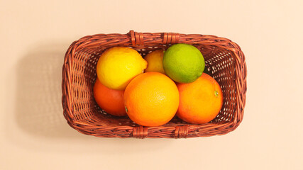 Wooden basket with fresh citrus fruits on pastel beige backgrund. Flat lay summer food