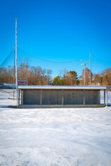 Baseball field with fenced dugout in frozen snow on a bright sunny day